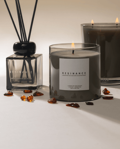 Two candles and one reed diffuser with 'Resinance' branding on a white surface with amber and resin decor on neutral background.