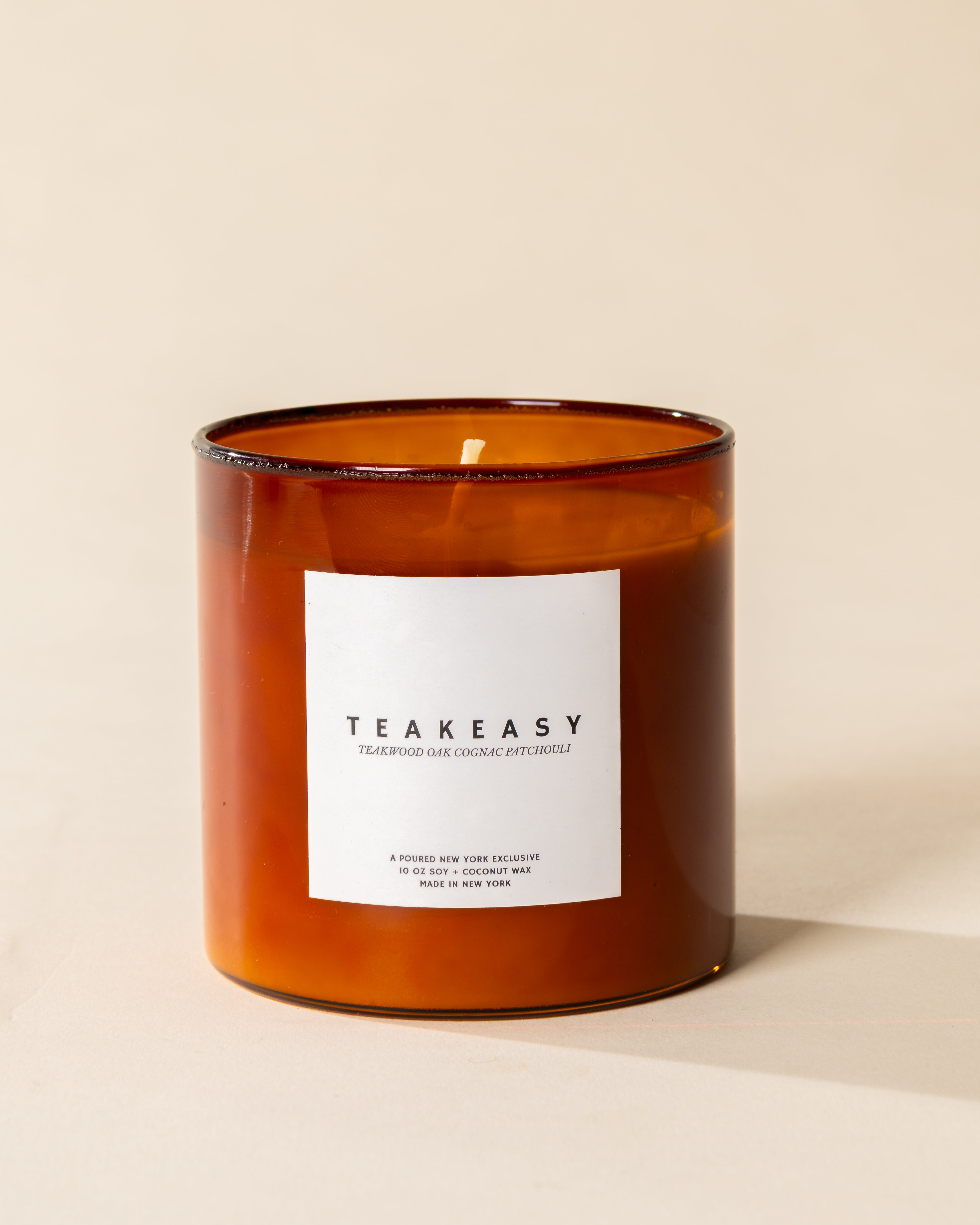 Poured New York 'Teakeasy' 10 oz amber glass soy wax candle on a neutral background