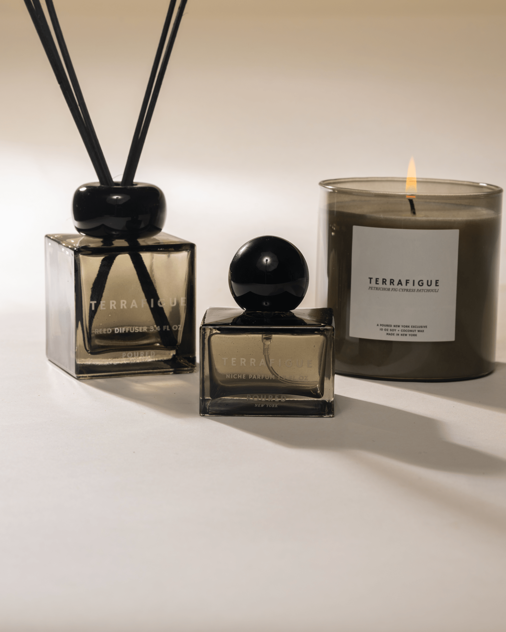 Olive green 'Terrafigue' diffuser, niche parfum, and candle lit on a neutral background
