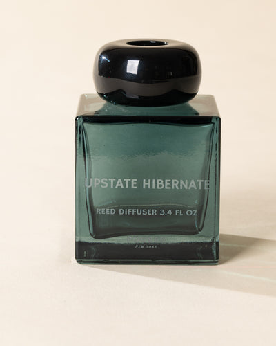 Poured New York 'Upstate Hibernate' reed diffuser in a teal glass vessel on a neutral background