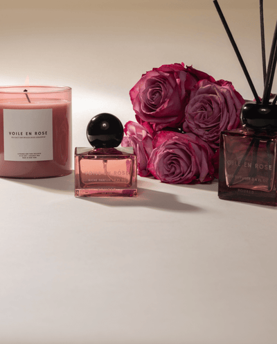 Poured New York 'Voile en Rose' pink glass candle, niche parfum, and reed diffuser with a pink rose bouquet on neutral background