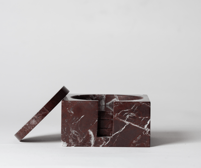 Dark Red Marble Square Coaster Set that comes with four matching dark red marble coasters with one of the coasters leaning on the coaster set on a neutral background.