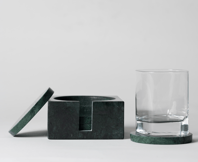 Moss Green Marble Square Coaster Set that comes with four matching moss green marble coasters on a neutral background with a clear cocktail glass sitting on one of the coasters. 