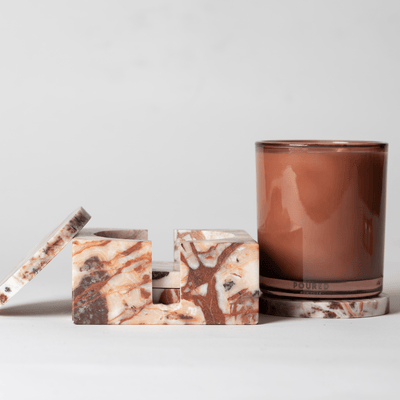 Brick Marble Coaster Set with four coasters sitting next to a matching glass candle vessel sitting on top of one of the coasters on a neutral background.