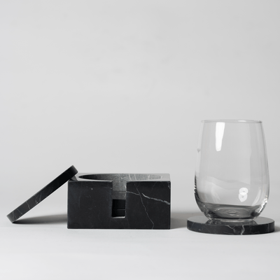 Noir Marble Square Coaster Set that comes with four matching noir marble coasters on a neutral background with a clear stemless wine glass sitting on top of a coaster.