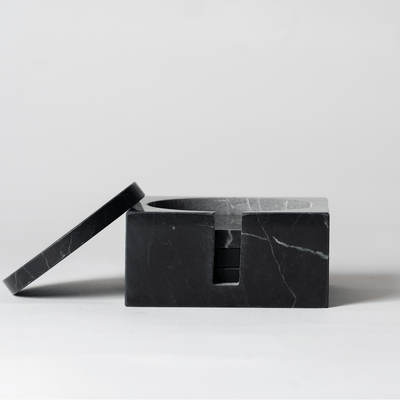 Noir Marble Square Coaster Set that comes with four matching noir marble coasters with one of the coasters tilted on the holder on a neutral background.